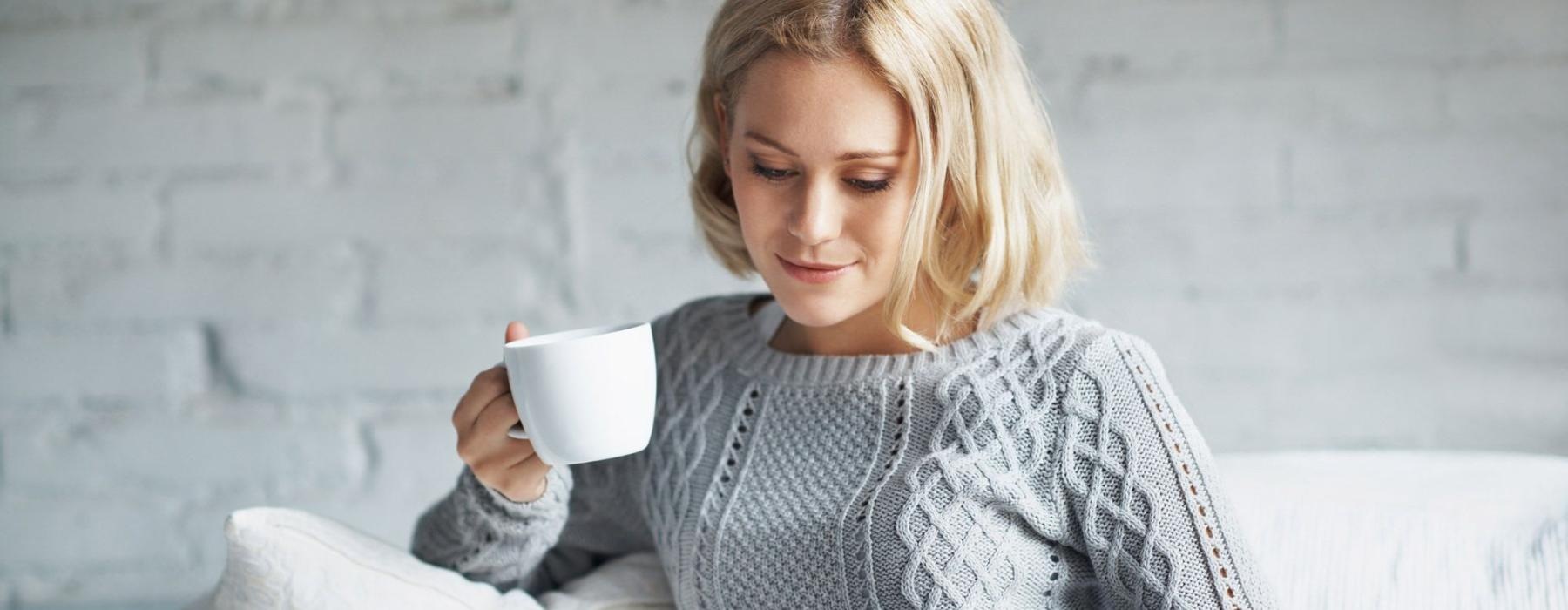 a woman sits on a couch with a cup of coffee and looks at her tablet